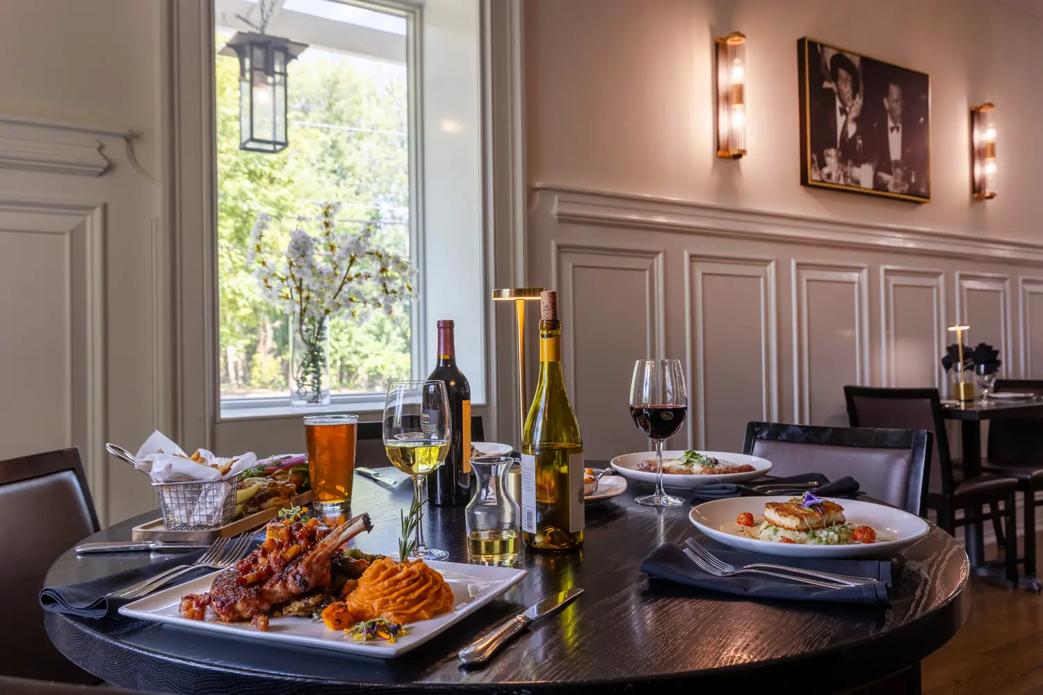 Table of plated entrees with wine by the window at The Squire Restaurant in West Long Branch NJ